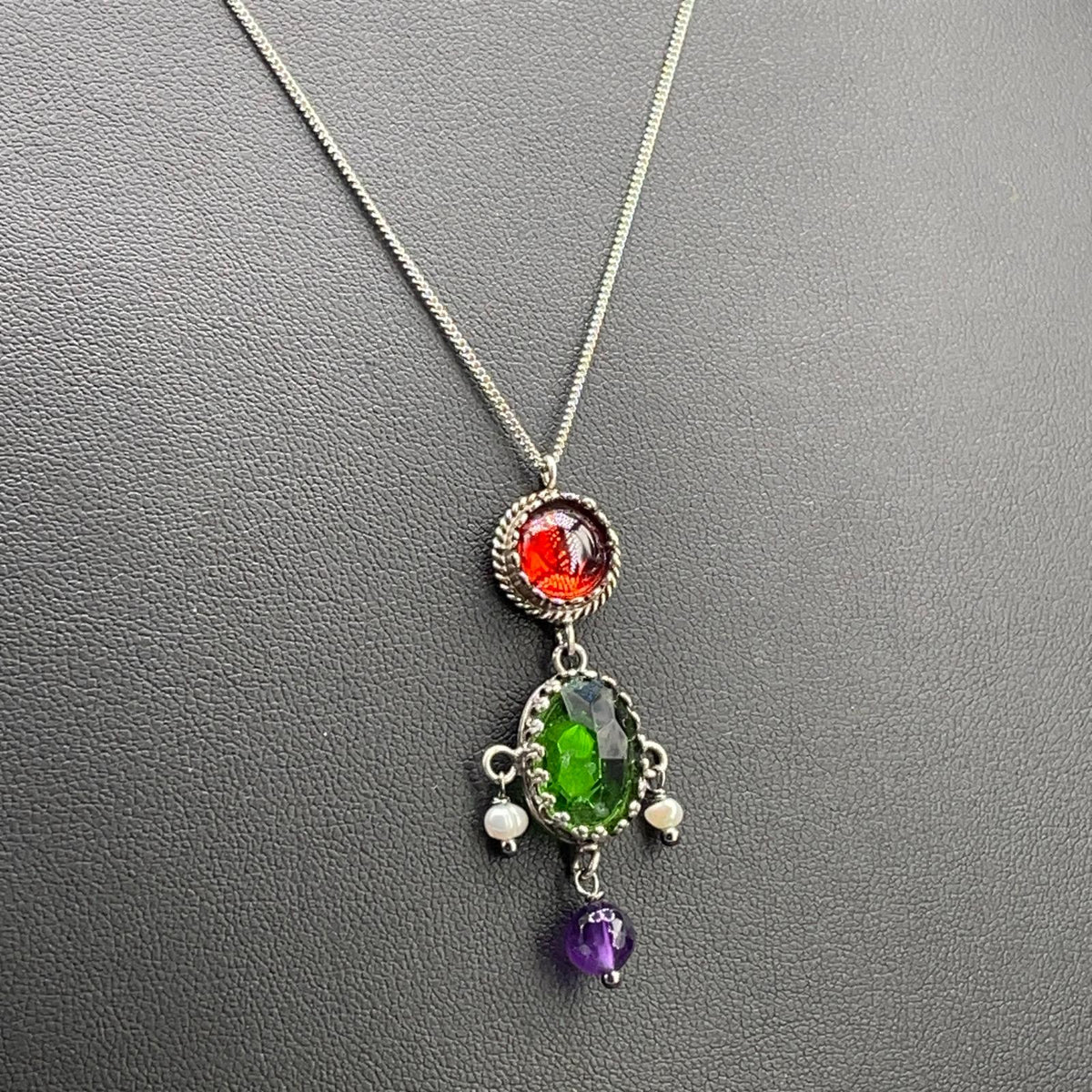 Dettaglio del pendente BonBon in argento 925 con pietra ovale verde sfaccettata e piccolo elemento viola