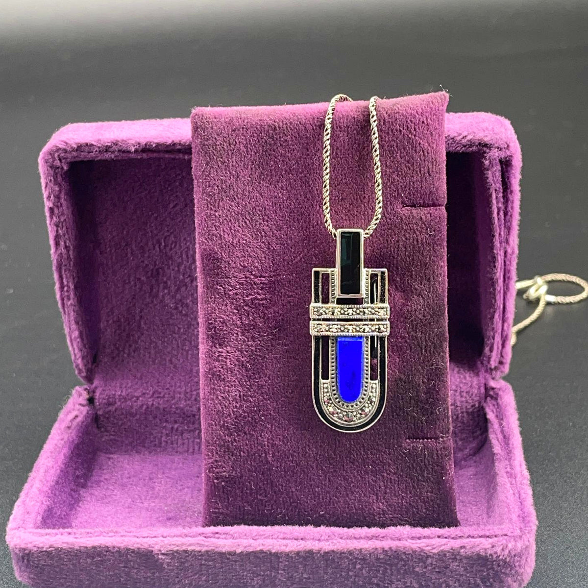 Collana in argento 925 con pendente di lapislazzuli blu e onice, esposta su velluto viola