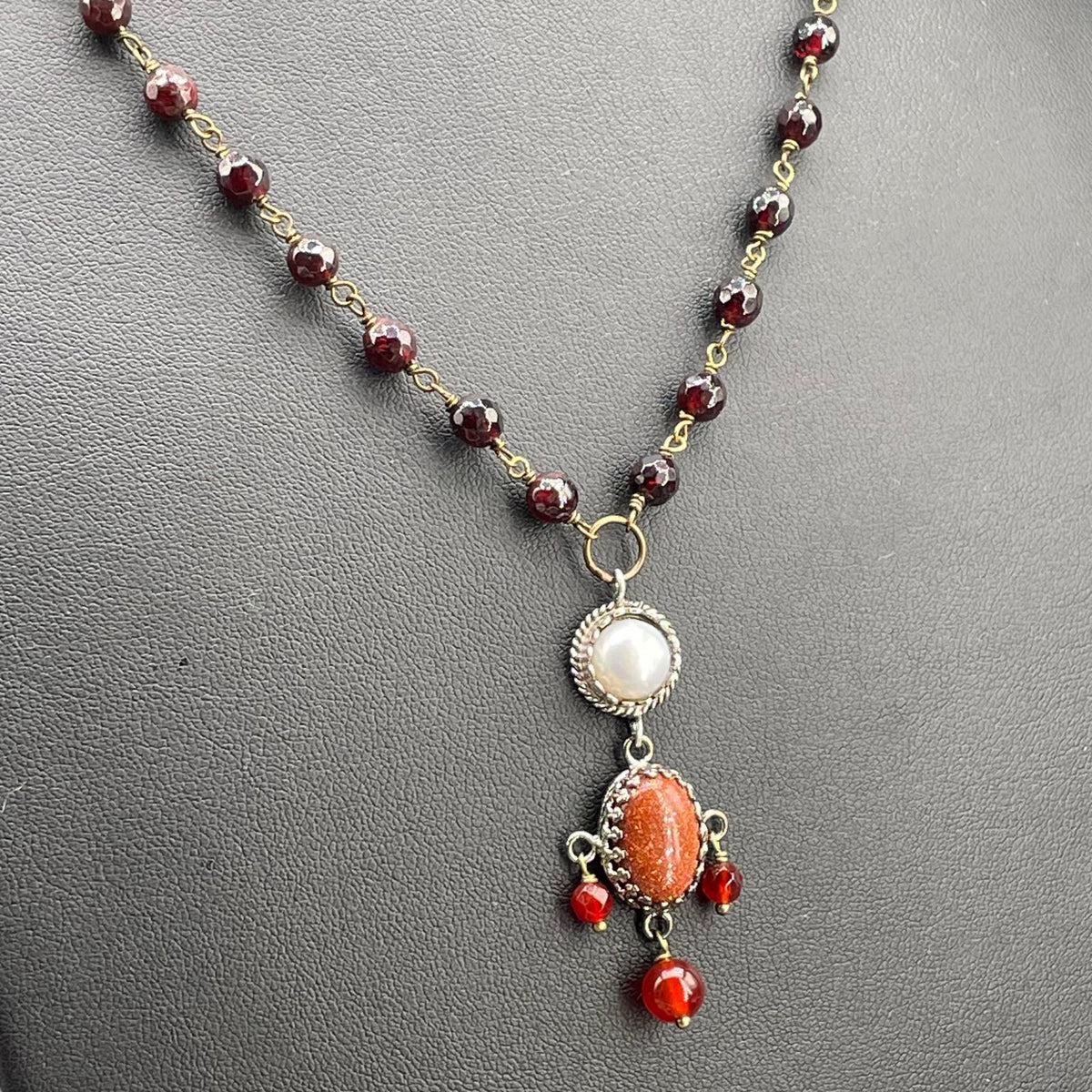 Dettaglio del pendente arancio con perla coltivata e gocce rosse