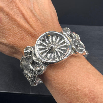 Bracciale rigido in argento elettroformato indossato su polso sottile con medaglione decorativo al centro