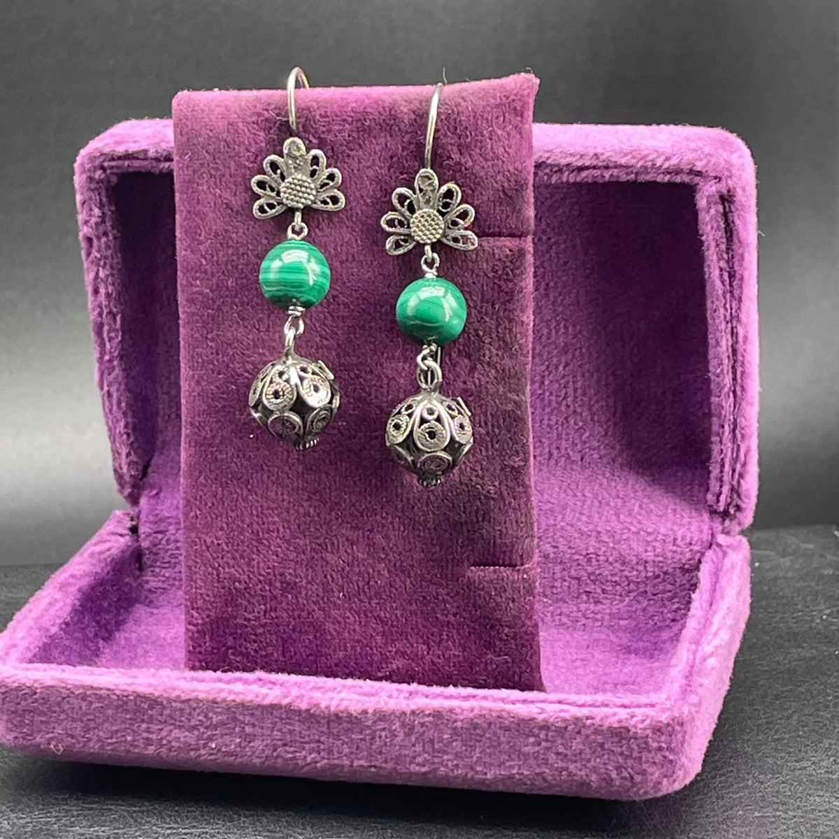 Orecchini con malachite esposti su supporto in velluto viola